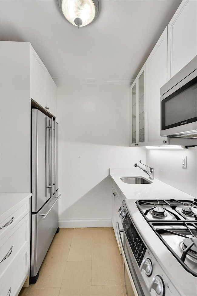 Kitchen featuring appliances with stainless steel finishes, a sink, glass insert cabinets, and white cabinetry