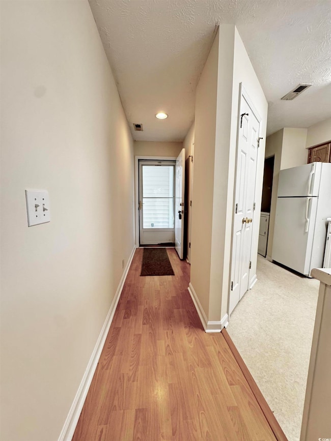 Corridor with light wood finished floors, baseboards, and a textured ceiling