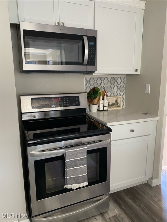 Kitchen with stove, white cabinetry, dark wood-style flooring, and backsplash