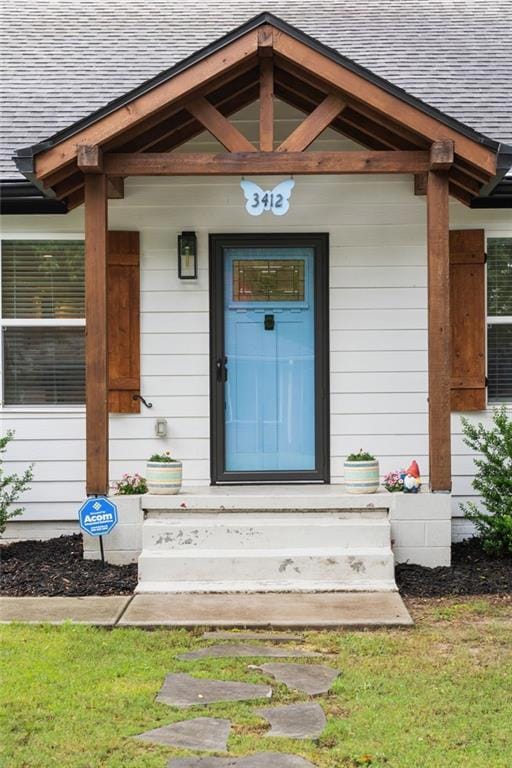 View of exterior entry with a shingled roof