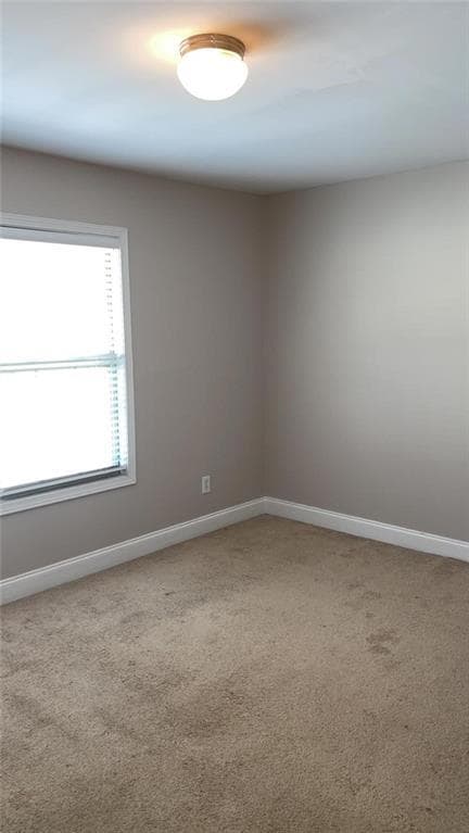 Carpeted spare room featuring baseboards