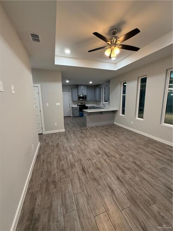 Unfurnished living room featuring ceiling fan, dark hardwood / wood-style flooring, a tray ceiling, and sink