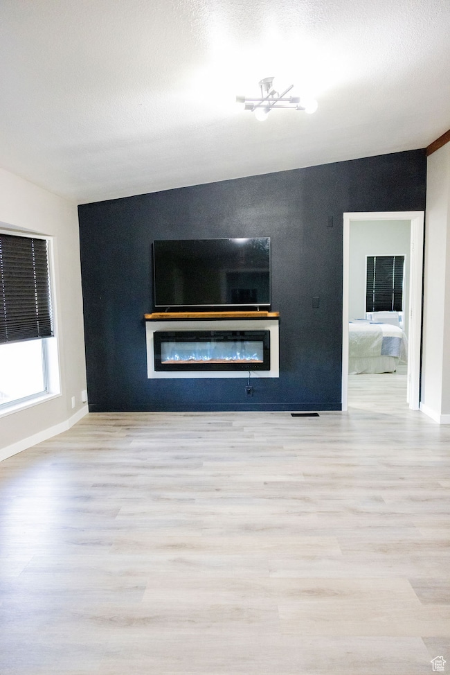 Unfurnished living room featuring light wood-type flooring, a glass covered fireplace, and a textured ceiling