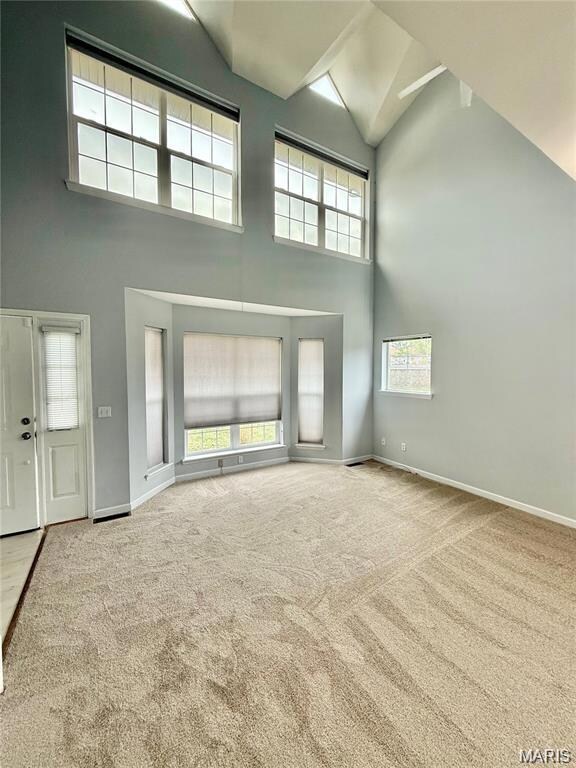 Unfurnished living room with high vaulted ceiling and light carpet