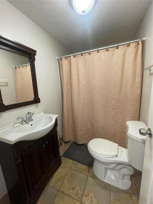 Bathroom featuring tile patterned flooring, vanity, a textured ceiling, and toilet
