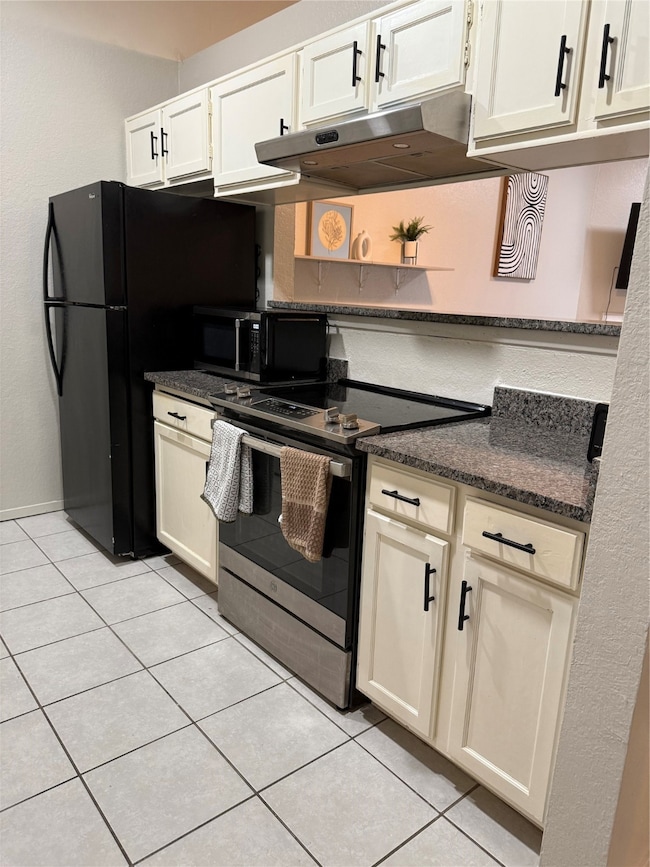 Kitchen featuring range with electric cooktop, extractor fan, light tile patterned floors, stainless steel microwave, and white cabinets