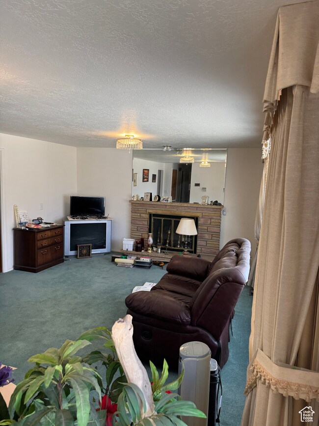 Carpeted living room with a stone fireplace and a textured ceiling