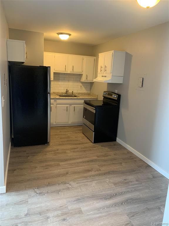 Kitchen with appliances with stainless steel finishes, tasteful backsplash, white cabinetry, light wood finished floors, and under cabinet range hood