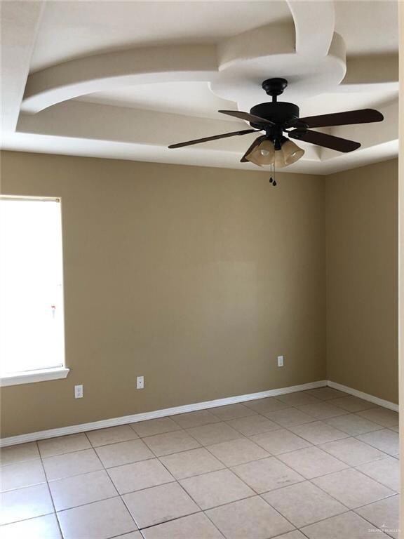 Empty room featuring light tile patterned floors, a ceiling fan, and baseboards