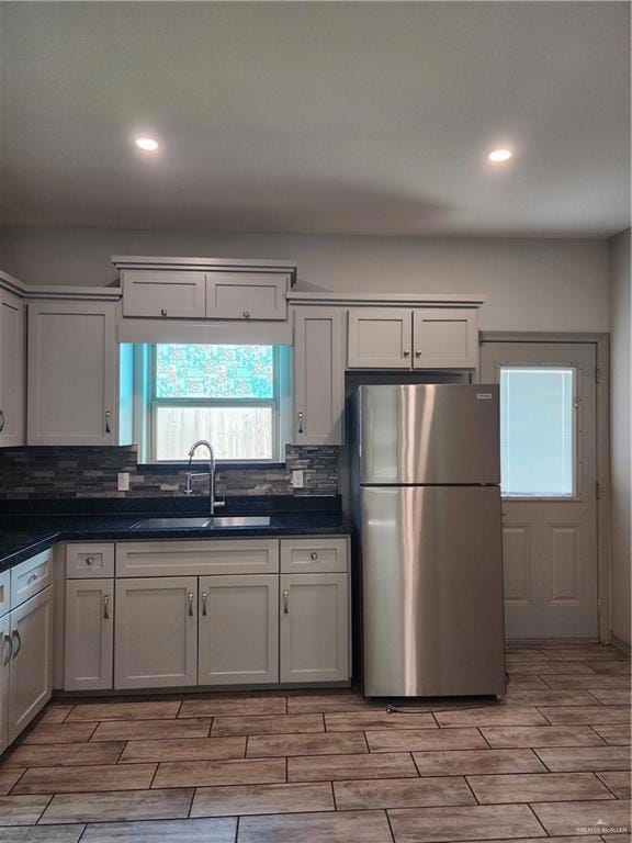 Kitchen featuring refrigerator, light wood-style floors, dark countertops, decorative backsplash, and recessed lighting