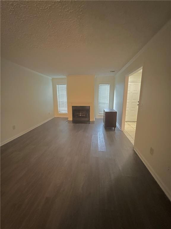 Unfurnished living room with dark wood-type flooring, a textured ceiling, a fireplace with flush hearth, crown molding, and healthy amount of natural light