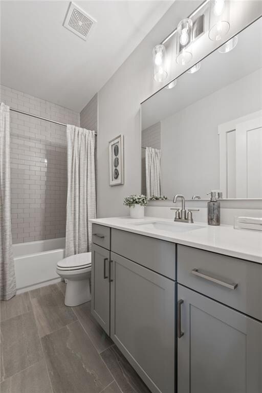 Full bath featuring toilet, vanity, visible vents, and shower / bathtub combination with curtain