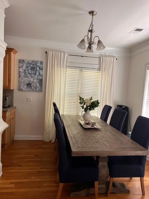 Dining space featuring a chandelier, light wood-type flooring, crown molding, and healthy amount of natural light