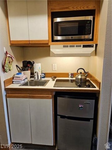 Kitchen featuring stainless steel microwave, under cabinet range hood, black electric stovetop, and white cabinetry