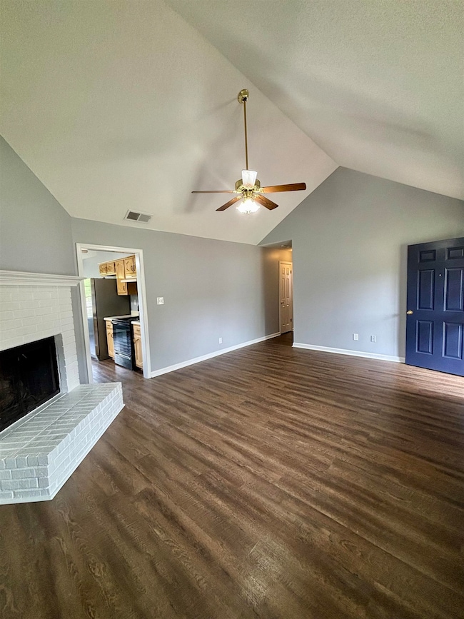 Unfurnished living room featuring vaulted ceiling, ceiling fan, a fireplace, dark wood-style floors, and baseboards