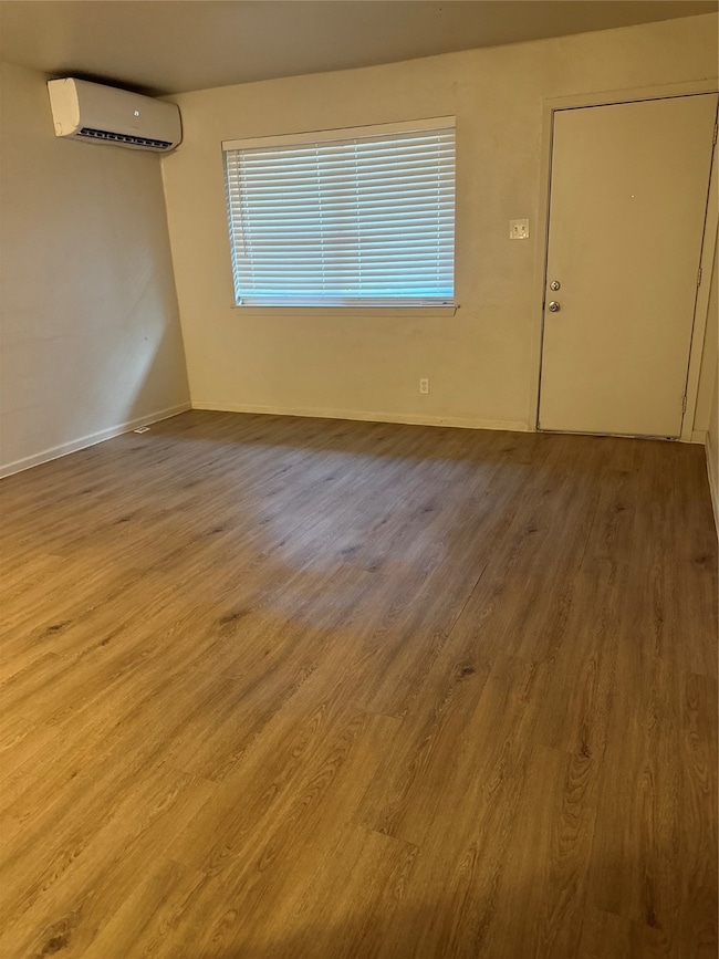 Empty room featuring light wood-style flooring and an AC wall unit