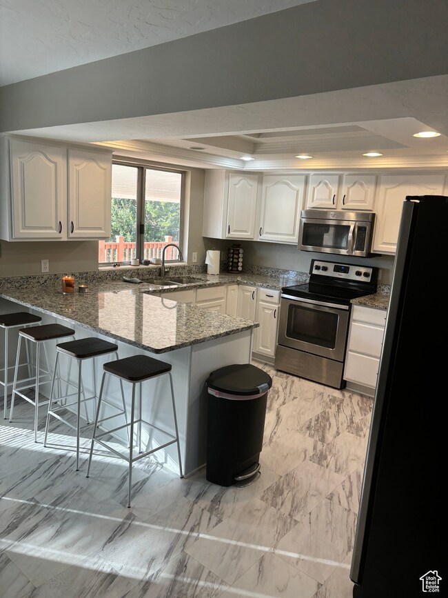 Kitchen featuring granite counters, a kitchen bar, kitchen peninsula, white cabinetry, and stainless steel appliances