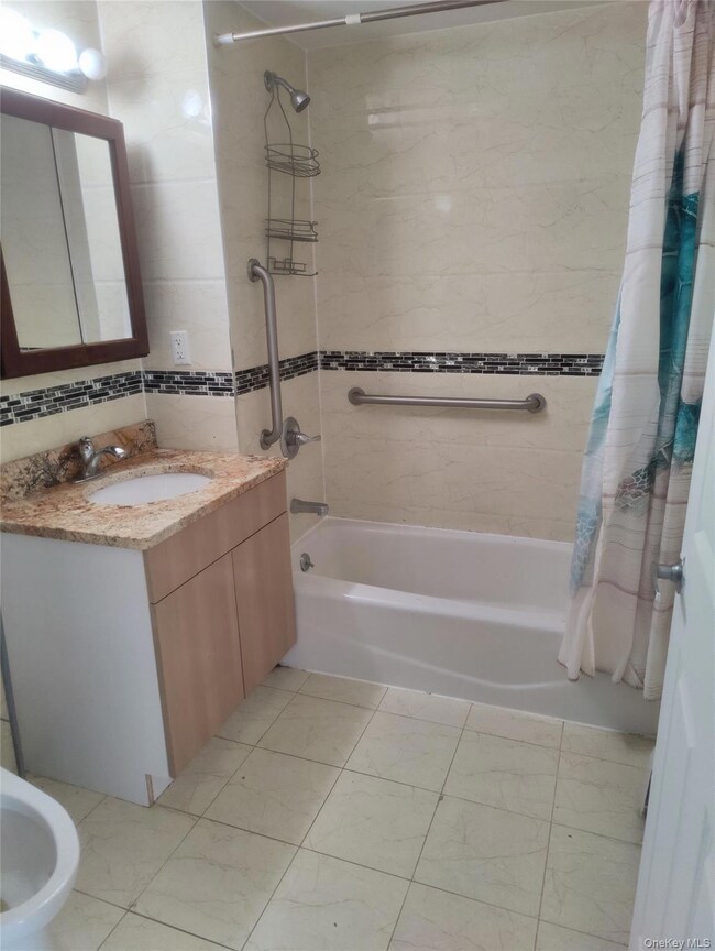 Bathroom featuring shower / bath combination with curtain, vanity, a bidet, tile walls, and light tile patterned floors