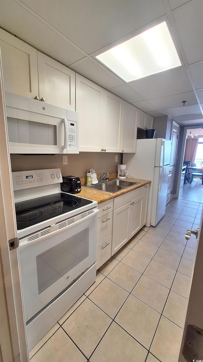 Kitchen with white appliances, white cabinets, light tile patterned flooring, light countertops, and a paneled ceiling