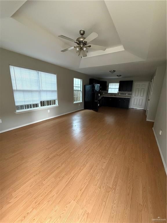 Unfurnished living room with a raised ceiling, wood finished floors, a ceiling fan, and baseboards