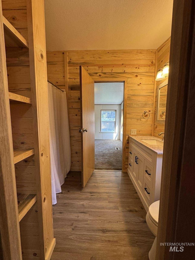 Full bath featuring vanity, dark wood-style flooring, a textured ceiling, a shower with shower curtain, and wood walls