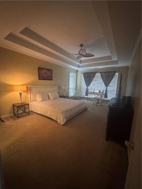 Carpeted bedroom with a tray ceiling, crown molding, baseboards, and a ceiling fan