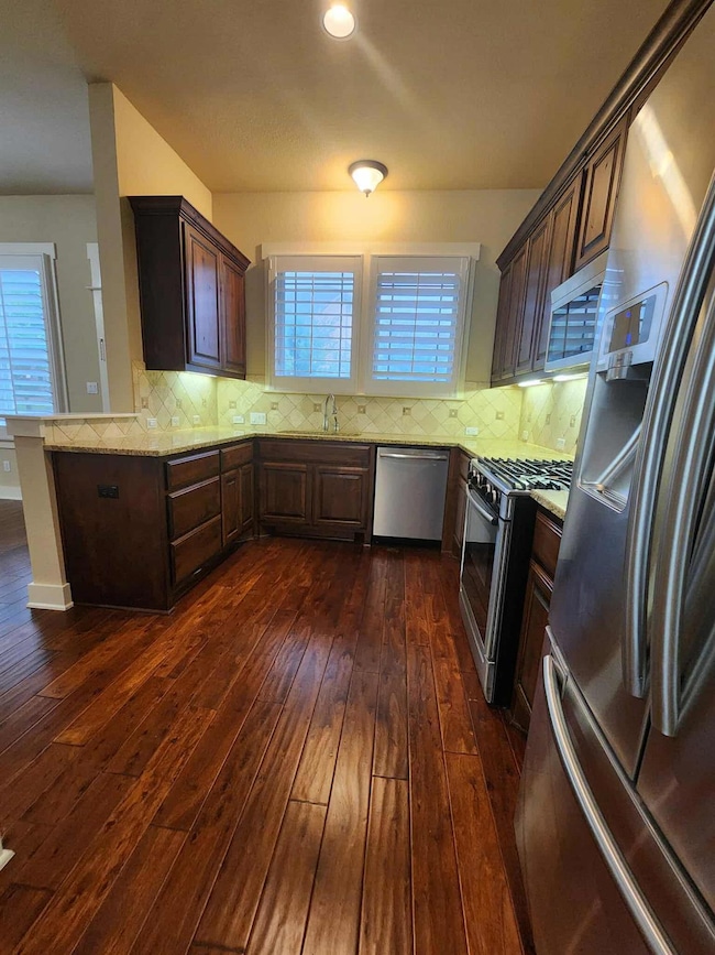 Kitchen featuring dark brown cabinets, stainless steel appliances, tasteful backsplash, and dark wood-type flooring