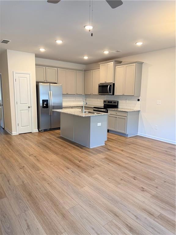 Kitchen with gray cabinetry, stainless steel fridge, an island with sink, and recessed lighting