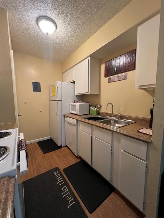 Kitchen with white microwave, a sink, a textured ceiling, light wood-type flooring, and dishwashing machine