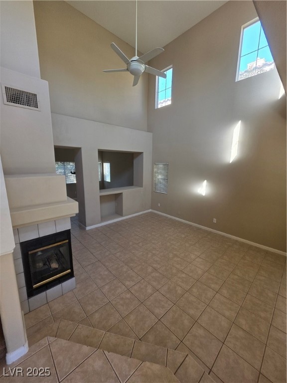 Unfurnished living room featuring high vaulted ceiling, a glass covered fireplace, light tile patterned floors, a ceiling fan, and built in shelves