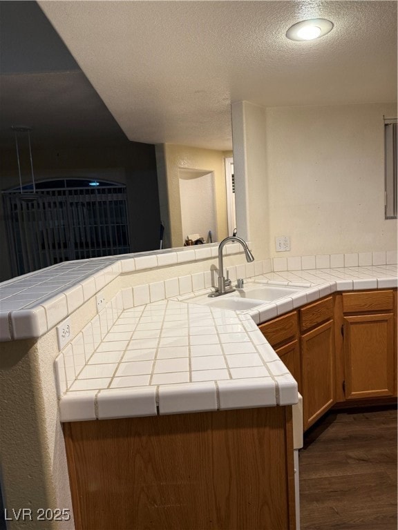 Kitchen featuring a sink, tile counters, dark wood