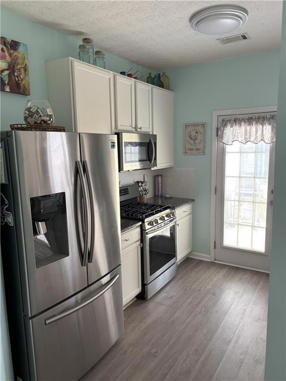 Kitchen with appliances with stainless steel finishes, a textured ceiling, white cabinets, dark wood-style floors, and dark stone countertops
