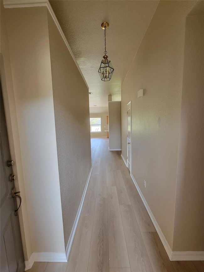 Hall with light wood-type flooring and a chandeli