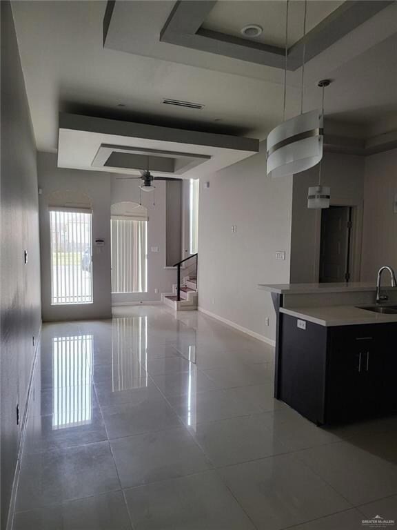 Kitchen with a tray ceiling, tile patterned flooring, a ceiling fan, and dark cabinetry