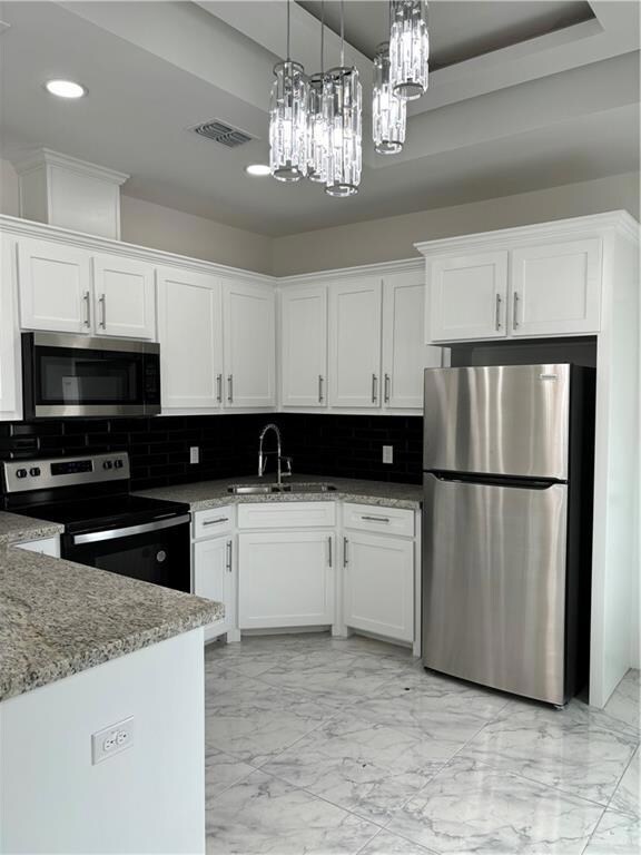 Kitchen with sink, stove, a notable chandelier, refrigerator, and white cabinetry