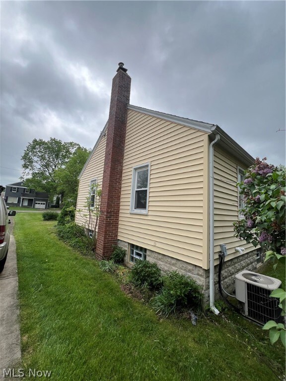 View of side of property with a yard and central air condition unit