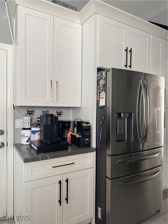 Kitchen featuring dark countertops, stainless steel refrigerator, white cabinetry, and light wood-type flooring