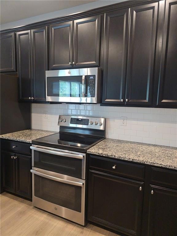 Kitchen with stainless steel appliances, light stone countertops, backsplash, and light wood-style flooring