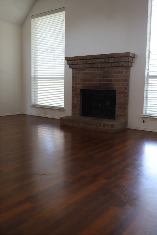 Unfurnished living room featuring a fireplace, dark wood finished floors, and vaulted ceiling