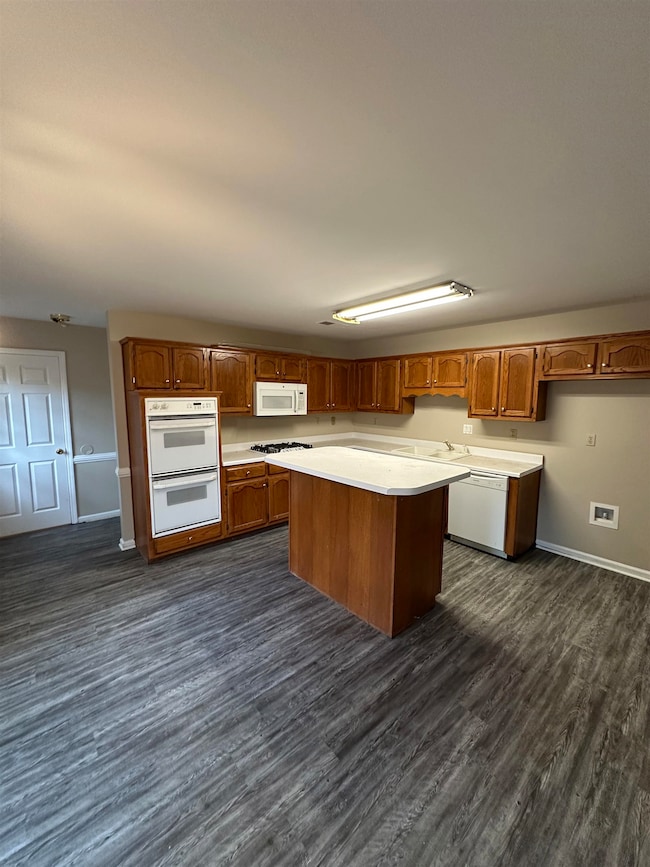 Kitchen with dark wood finished floors, white appliances, light countertops, a kitchen island, and brown cabinetry