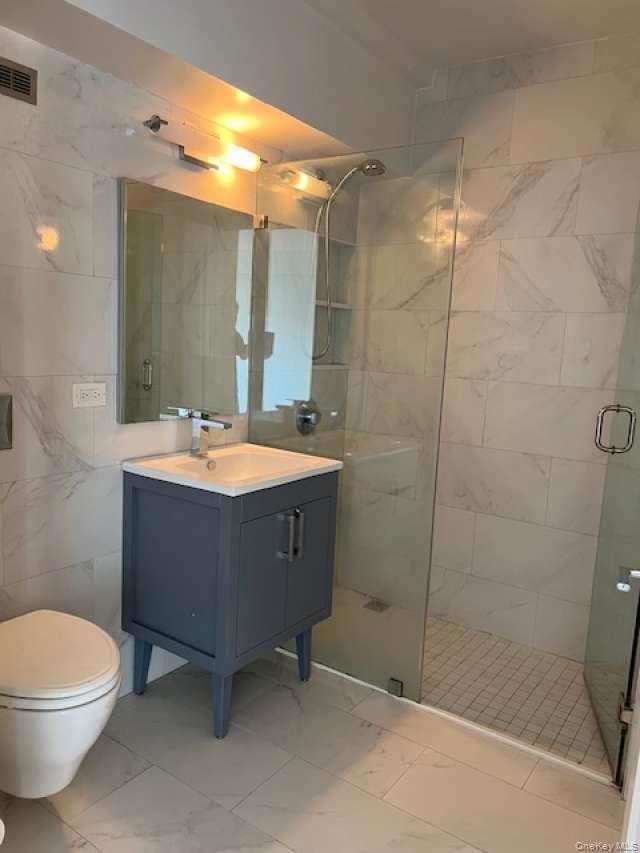 Bathroom featuring a shower stall, vanity, and tile walls