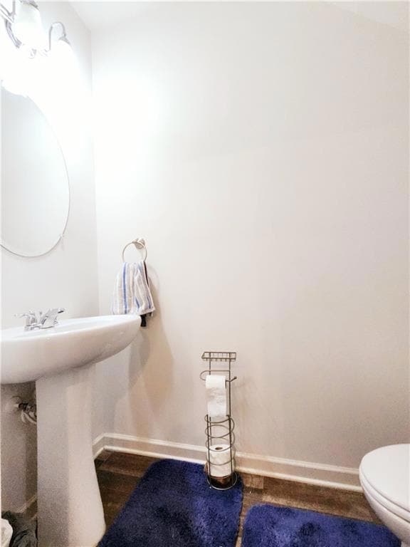 Half bath with baseboards, a sink, toilet, and wood finished floors