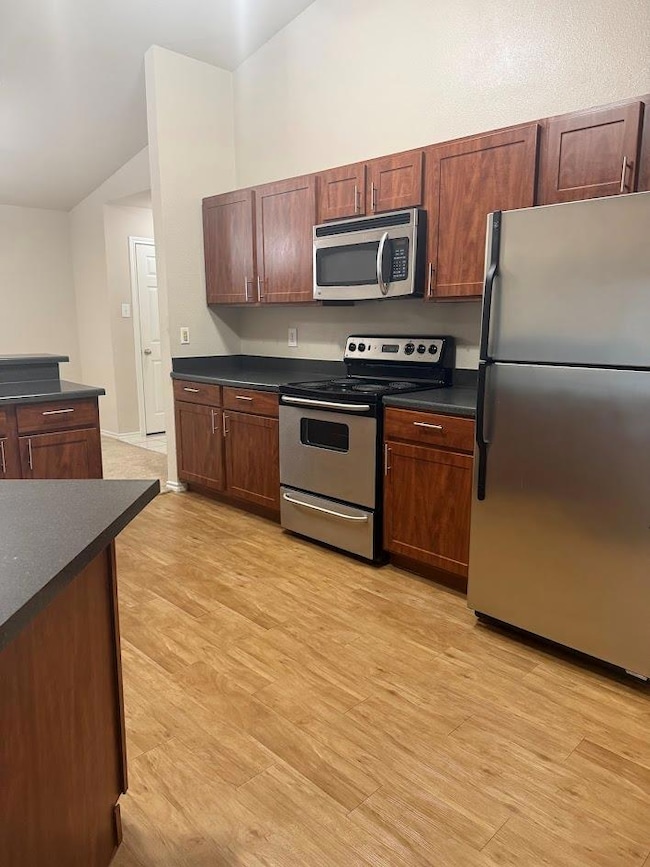 Kitchen with appliances with stainless steel finishes, dark countertops, lofted ceiling, and light wood-type flooring