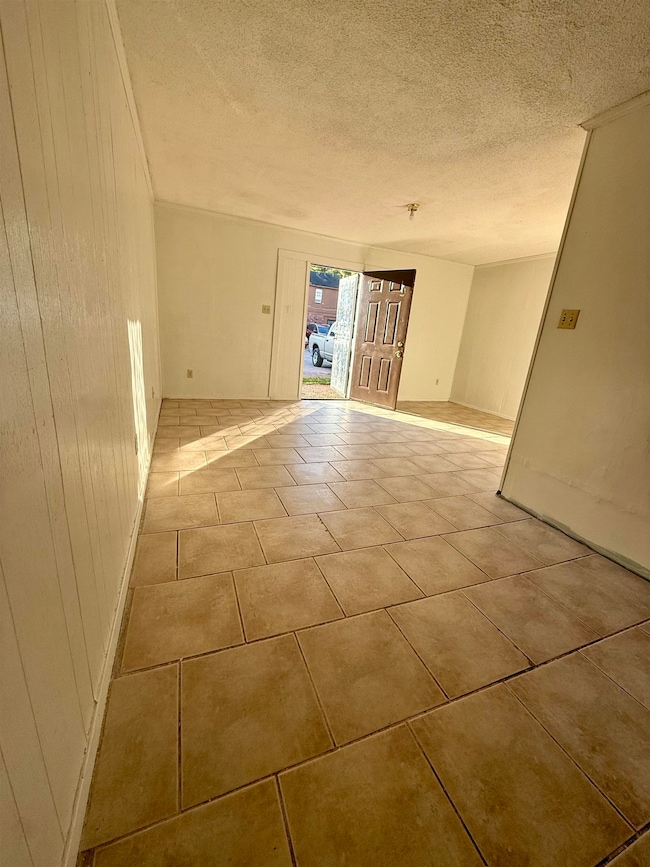 Empty room with a textured ceiling, light tile patterned floors, and wooden walls