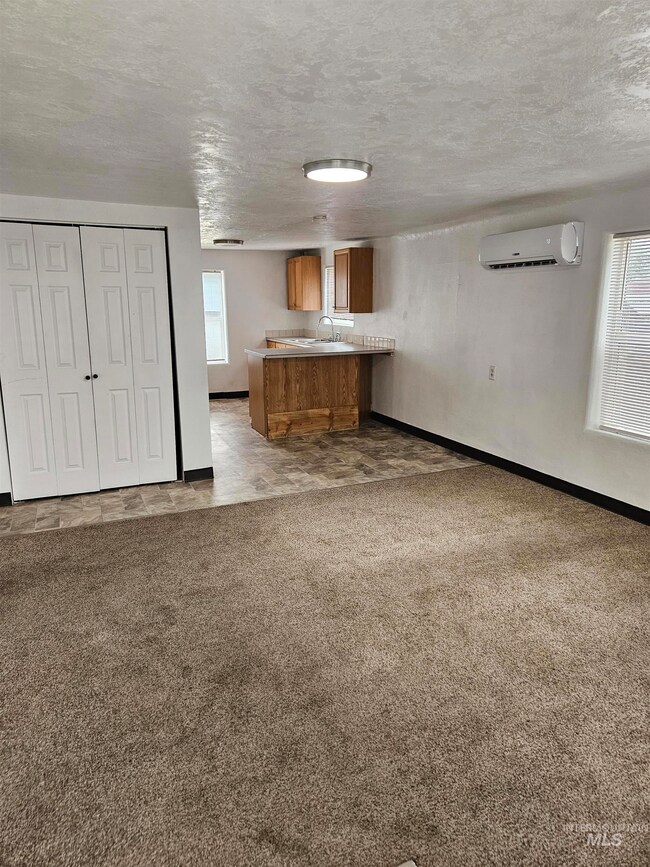 Unfurnished living room featuring an AC wall unit, carpet floors, and a textured ceiling