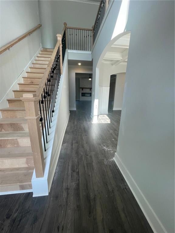 Stairway with arched walkways, wood finished floors, baseboards, a towering ceiling, and beamed ceiling