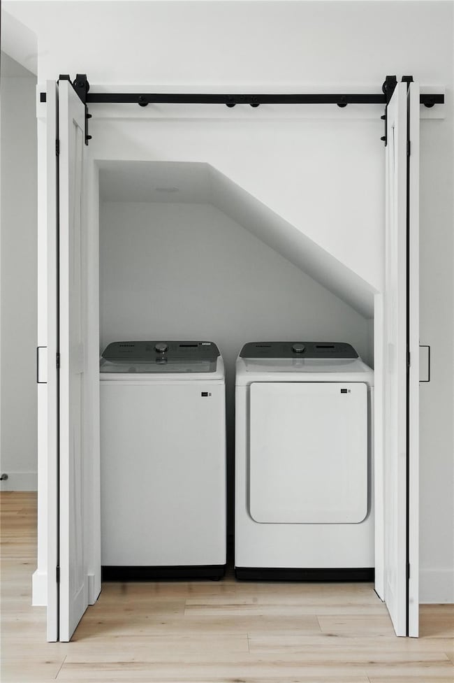 Washroom featuring light wood finished floors, a barn door, and washer and clothes dryer