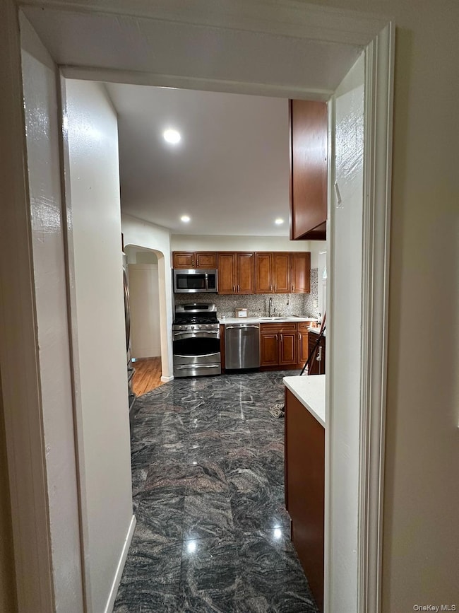 Kitchen featuring arched walkways, brown cabinets, stainless steel appliances, dark marble finish floors, and recessed lighting