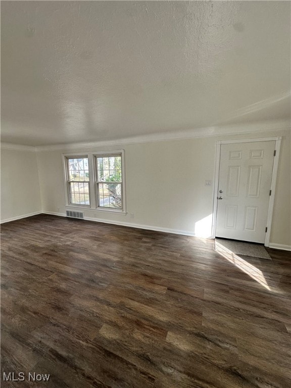 Empty room with dark wood finished floors, a textured ceiling, and crown molding