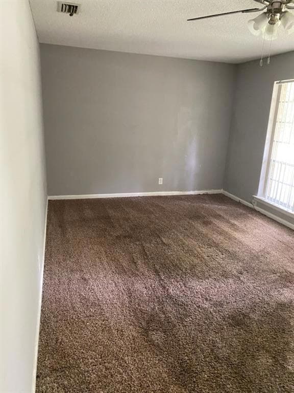 Empty room with dark carpet, a textured ceiling, and ceiling fan